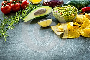 Guacamole bowl with ingredients and tortilla chips on a stone table. Selective focus. Copyspace for your text.