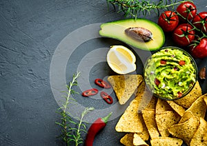 Guacamole bowl with ingredients and tortilla chips on a stone table. Top view image. Copyspace for your text.