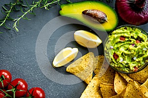 Guacamole bowl with ingredients and tortilla chips on a stone table. Top view image. Copyspace for your text.