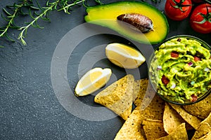 Guacamole bowl with ingredients and tortilla chips on a stone table. Top view image. Copyspace for your text.