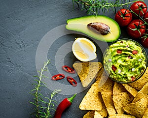 Guacamole bowl with ingredients and tortilla chips on a stone table. Top view image. Copyspace for your text.