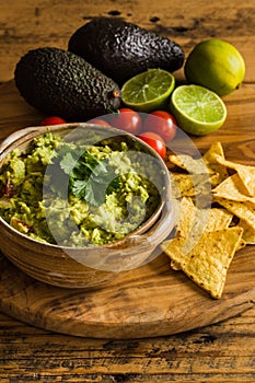 Guacamole dip in a bowl with scattered tortilla chips tomatoes avocados and limes