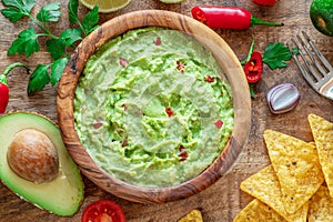 Guacamole, guacamole ingredients and chips on wooden background. Flat lay