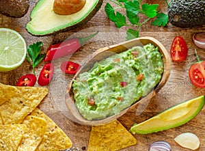 Guacamole, guacamole ingredients and chips on wooden background. Flat lay