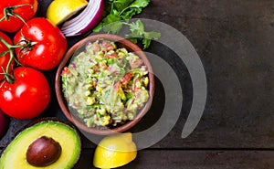 Guacamole and ingredients - avocado, tomatoes, onion, cilantro dark background.