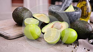 guacamole ingredients - Avocados, limes whole and cut on concrete table with a marble mortar