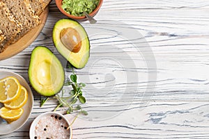 Guacamole ingredients on wooden table, avocado, salt and pepper, lemon, spices and whole grain bread for toasts