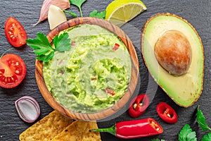 Guacamole sauce and guacamole ingredients, popular Mexican food, on slate serving board. Top view