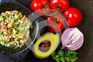 Guacamole in stone mortar and ingredients avocado, tomatoes, onion, cilantro
