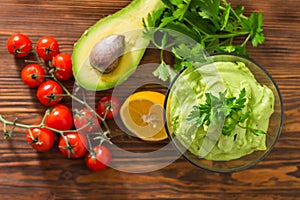 Guacamole on wooden table surrounded by its ingridients