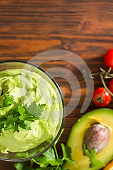 Guacamole on wooden table surrounded by its ingridients