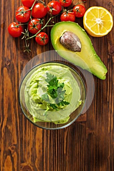Guacamole on wooden table surrounded by its ingridients