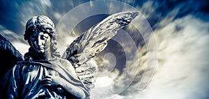 Guardian angel sculpture with open long wings  with blurred white clouds dramatic light blue sky. Angel sad expression