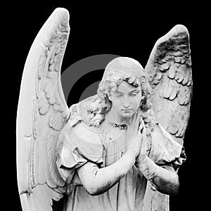 Guardian angel sculpture with open wings isolated on black background. Angel sad expression sculpture with eyes down and hands