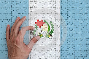Guatemala flag is depicted on a puzzle, which the man`s hand completes to fold