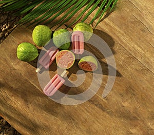 Guava Popsicle with grava fruits on a wood base, sunlight, palm leaf, top view photo