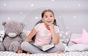 Guess her favorite fairy tale. Girl child sit bed with teddy bear read book. Kid prepare to go to bed. Pleasant time in