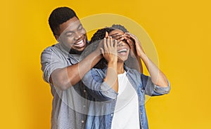 Guess who. Affectionate black man surprising his wife, covering her eyes