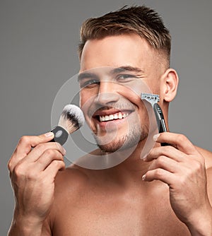 Guess whos getting rid of the beard. Studio shot of a handsome young man holding a razor and brush against a grey