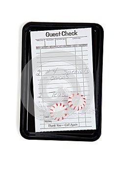 A guest check on a tip tray with mints on white