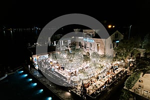 Guests sit at festive tables in the courtyard of the Adriatica Hotel at night under the light of garlands of light bulbs photo