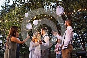 Guests with smartphones taking photo of bride and groom at wedding reception outside.