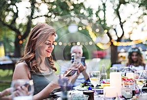 Guests with smartphones taking photo at wedding reception outside.