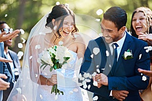 Guests throwing confetti over bride and groom as they walk past after their wedding ceremony. Joyful young couple