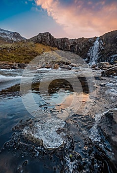 Gufufoss waterful with colorful clouds reflection on the frozen icy water