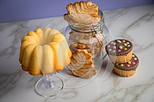 Gugelhupf ring cake, muffins, Italian puff pastry fan wavers cookies biscuits as selection buffet on marble table and lilac
