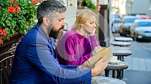 Guide to dating. Meeting people with similar interests. Man and woman sit cafe terrace. Girl interested what he reading