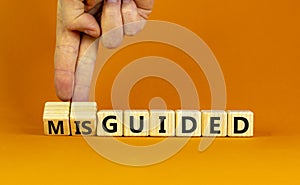 Guided or misguided symbol. Businessman turns wooden cubes and changes the word misguided to guided. Beautiful orange table,