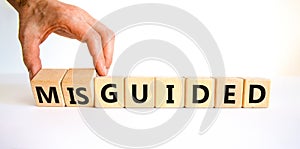 Guided or misguided symbol. Businessman turns wooden cubes and changes the word misguided to guided. Beautiful white table, white