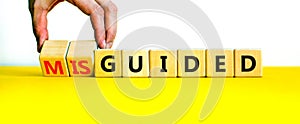 Guided or misguided symbol. Businessman turns wooden cubes and changes the word misguided to guided. Beautiful yellow table, white