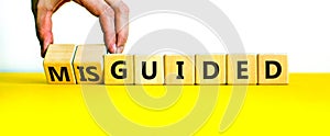 Guided or misguided symbol. Businessman turns wooden cubes and changes the word misguided to guided. Beautiful yellow table, white