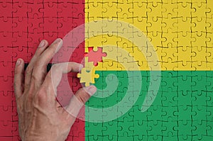 Guinea Bissau flag is depicted on a puzzle, which the man`s hand completes to fold