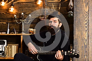 Guitar as hobby. Man bearded musician enjoy evening with bass guitar, wooden background. Man with beard holds black