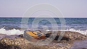 Guitar on the beach ashore of sea or ocean. Sea water or wave washes the guitar. Acoustic guitar ashore ocean with waves