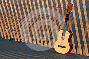 Guitar on beach fence with sunset illumination