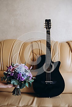 Guitar and the bouquet are on a leather sofa