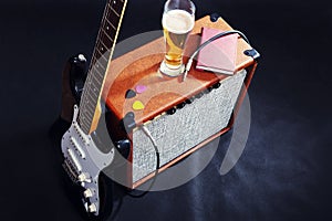 Guitar combo amplifier with black guitar, glass of beer and notepad on black background