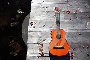 guitar on a dock in autumn with leaves and water (wood, color contrast acoustic autumn)