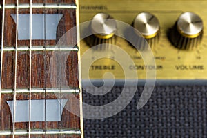 Guitar fretboard and fret marker detail, blurred old amplifier knobs in the background
