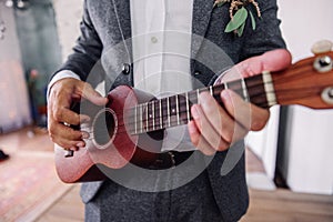 Guitar with hands of the groom, close-up. Ukulele, hands of the groom with wedding ring. Romance, love, family.
