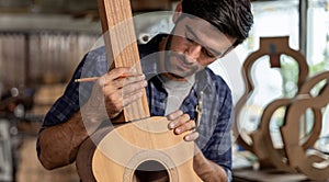 Guitar makers man making acoustic guitars in laboratory. Asian guitar maker builds high quality guitars for musicians handmade