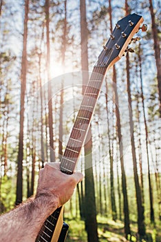 Guitar in a man hand against a blue sky - sunbeams through trees - open air rock festival