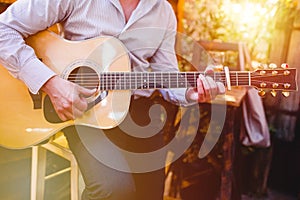 Guitar with a man`s male hands playing the guitar on wooden wall background, electric or acoustic guitar with nature light. Concep