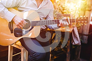Guitar with a man`s male hands playing the guitar on wooden wall background, electric or acoustic guitar with nature light. Concep
