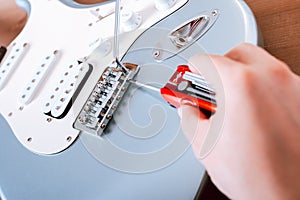 Guitar master adjusting bridge saddle on tremolo of electric guitar using multitool