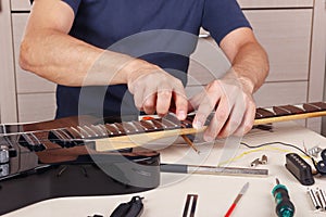 Guitar master burnishes the edge of frets on neck of guitar